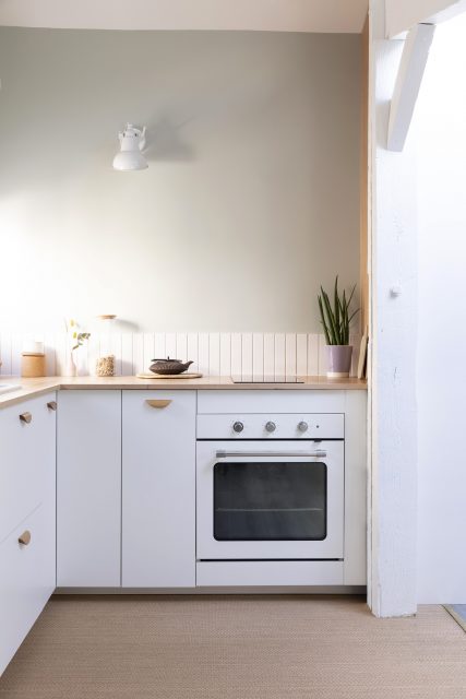 Vue sur la cuisine aux tonalités douces vert de gris, blanche et bois avec son sol tressé délimitant l'espace cuisine au sol, projet sous les toits Ribera Paris 16 .