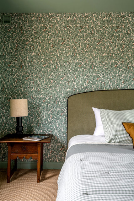 Réalisation rénovation et décoration par Ingrid Marcille. Chambre chaleureuse en maison secondaire, avec tête de lit en tissu vert et papier peint végétal, dans une maison de campagne en Normandie.